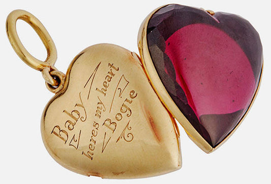 Vintage gold locket with heart-shaped ruby gemstone and engraved message 'Baby here's my heart Bogie' on the inside, symbolizing a romantic gesture.