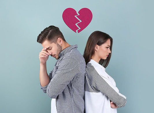 A man and woman standing back to back, symbolizing a breakup. A broken heart graphic is above them, representing emotional distance and relationship troubles.