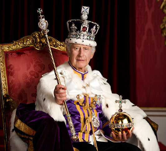 King Charles III sitting on the throne wearing royal attire, including the coronation crown, holding the orb and scepter, symbolizing his reign.