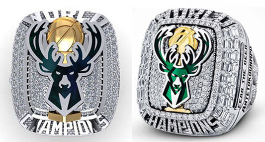 Close-up of the Milwaukee Bucks NBA Championship rings featuring a prominent antler logo and diamond embellishments. The rings showcase the team's iconic logo with intricate details, including a golden basketball and 'CHAMPIONS' inscription.