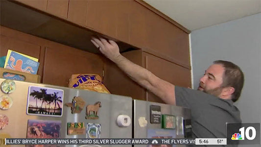 Man reaching for a bag of chips in a kitchen cabinet, with magnets on the refrigerator visible in the background.