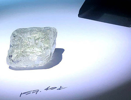 A 75.57-carat raw diamond shown under bright lighting, with the number '157.64' marked on the surface.