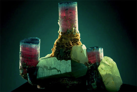 Close-up of a multi-colored crystal with red, pink, and green hues, showcasing a complex crystalline structure.