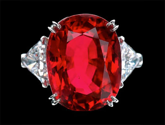 Close-up of a stunning red ruby ring with two sparkling diamond side stones, set in a white gold band, against a black background.