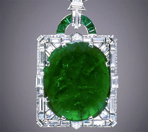 Close-up of a luxurious green jade pendant surrounded by a frame of sparkling diamonds. The pendant features an oval-shaped jade stone with a detailed geometric design, including baguette-cut diamonds and a unique jade loop at the top.