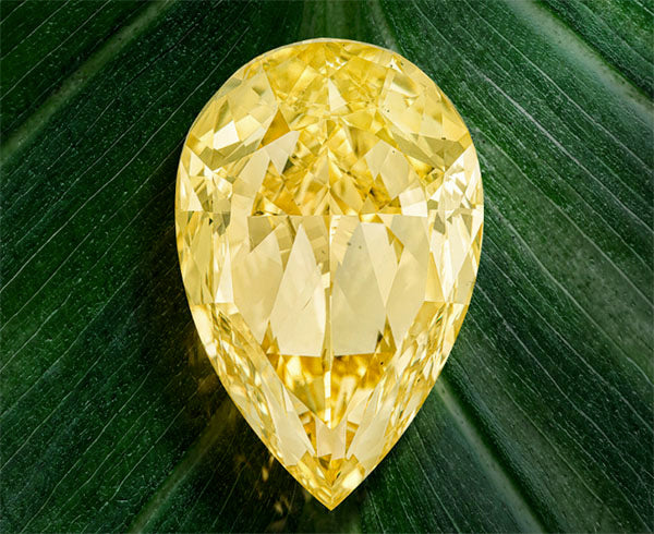 Large pear-shaped yellow diamond with intricate facets, resting on a green leaf background, showcasing brilliance and clarity.
