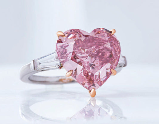 Close-up of a heart-shaped pink diamond engagement ring with side baguette diamonds on a white and rose gold band.