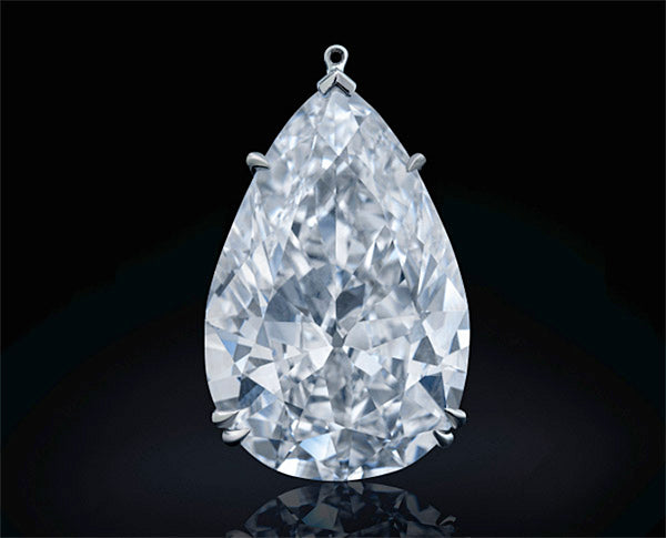 Large pear-shaped diamond pendant with intricate silver setting, reflecting light against a black background.