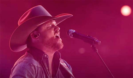 Country music singer wearing a cowboy hat, passionately performing with a guitar and microphone, captured in vibrant stage lighting during a live concert performance.
