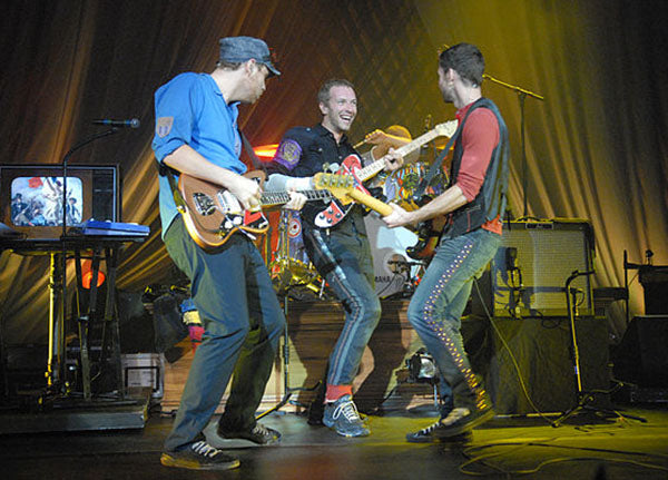 Coldplay band members performing live on stage, playing guitars and interacting during a concert.