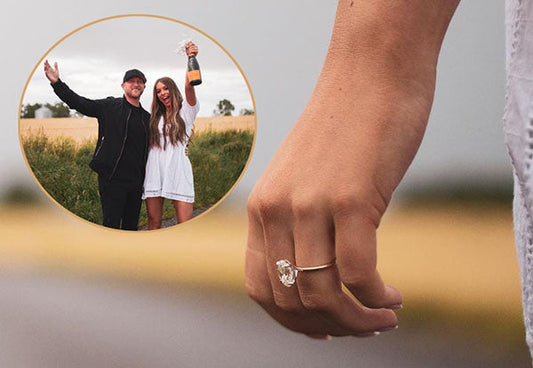 Engaged couple celebrating outdoors with a close-up of the engagement ring on the woman's hand, with the couple in the background holding champagne.