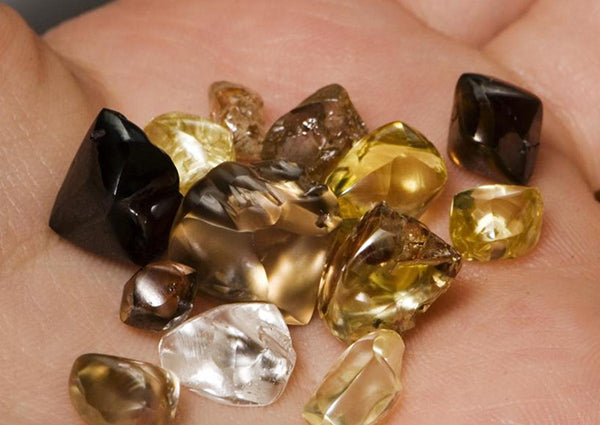 A hand holding a collection of various rough gemstones including black, brown, and yellow stones, showcasing different shapes and sizes.