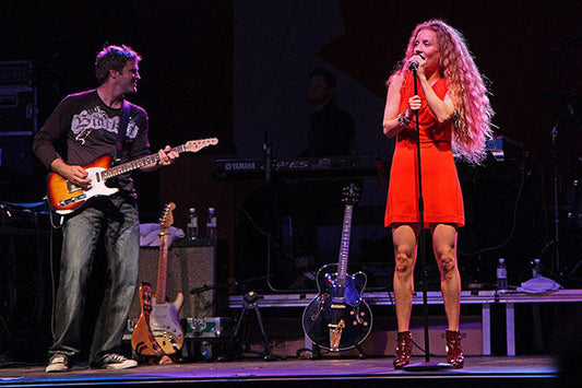 Female singer in a red dress performing on stage with a guitarist, live concert performance.