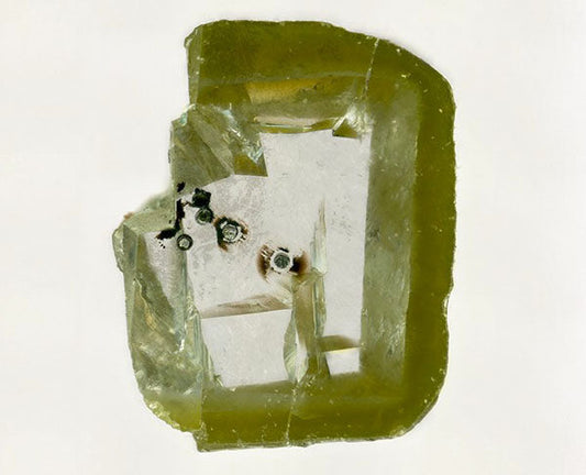 Close-up of a greenish-yellow gemstone with visible cracks and internal inclusions, showcasing its raw, unpolished form.
