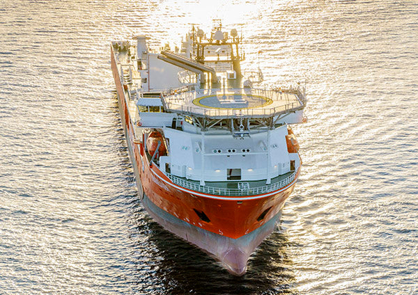 Aerial view of a large orange research or offshore oil rig vessel sailing on the water during sunset.