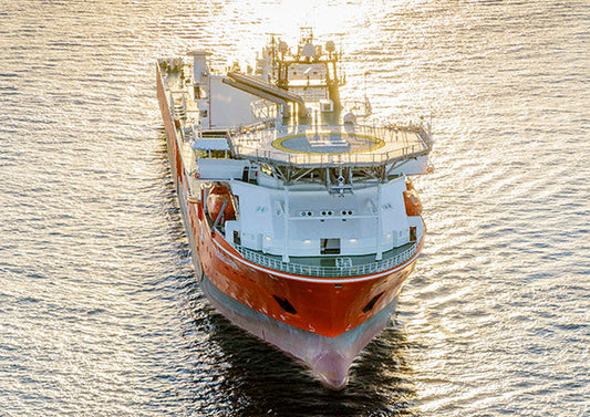 Aerial view of a large orange research or offshore oil rig vessel sailing on the water during sunset.