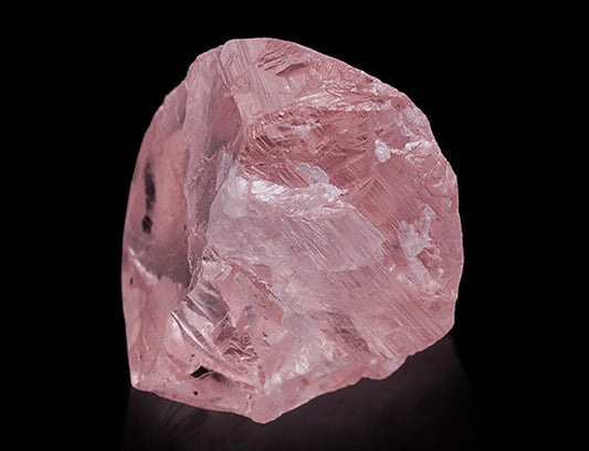 Large rough pink sapphire crystal with natural facets on a black background.