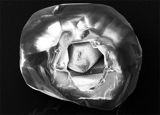 Close-up view of a broken diamond with a visible internal crack and rough inner structure captured in black and white.