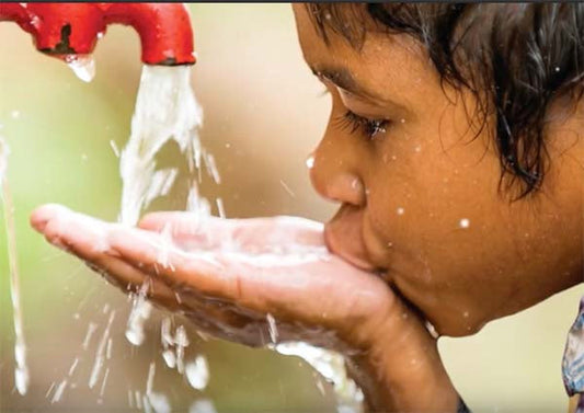 A child drinking water from their hands under a running faucet, capturing the refreshing moment as water flows gently.