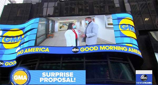 Large digital billboard displaying a surprise proposal segment from Good Morning America (GMA) with two people talking in a hallway and the GMA logo visible.