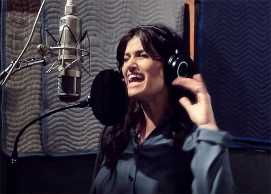 A singer recording vocals in a studio, wearing headphones and passionately singing into a microphone with studio soundproofing in the background.