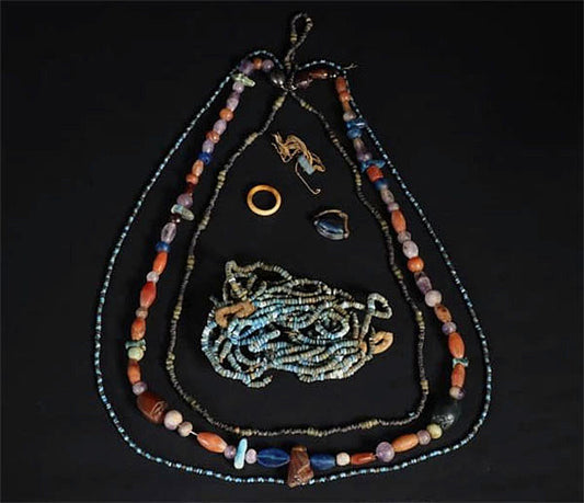 Collection of antique beads and jewelry pieces including necklaces, a ring, and small decorative objects arranged on a black background.