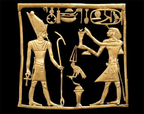 Ancient Egyptian gold artifact depicting two figures, one wearing a headdress and holding a scepter, the other offering a vessel, with hieroglyphic symbols above them.