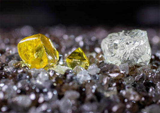 Raw yellow and clear diamonds placed on a bed of smaller rough diamonds.