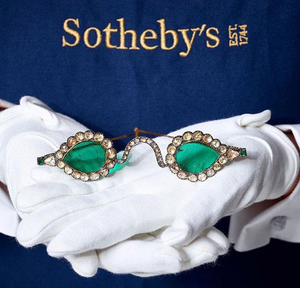 Vintage sunglasses with green lenses and diamond-studded frame held by a person wearing white gloves, with the Sotheby's logo visible on the background.