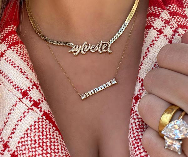 Close-up of layered gold necklaces with the words 'zybretel' and 'mama' in diamonds, complemented by a gold ring.