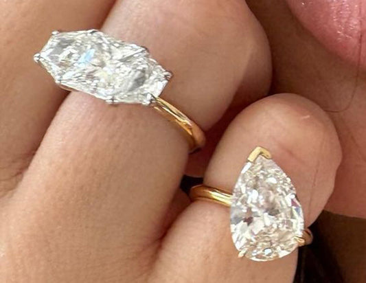 Two elegant diamond rings with pear-shaped stones set in gold bands, one larger than the other, worn on a person's fingers.