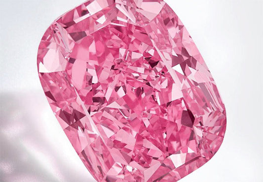 Close-up of a radiant pink diamond with a cushion cut, showcasing vibrant color and multiple facets reflecting light.