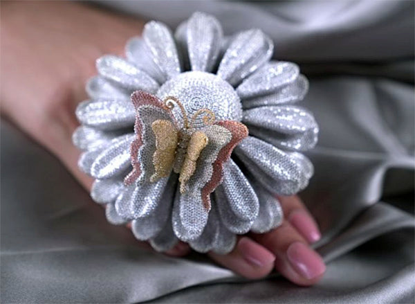 Close-up of a silver flower-shaped brooch with a butterfly design in the center, held in a hand.