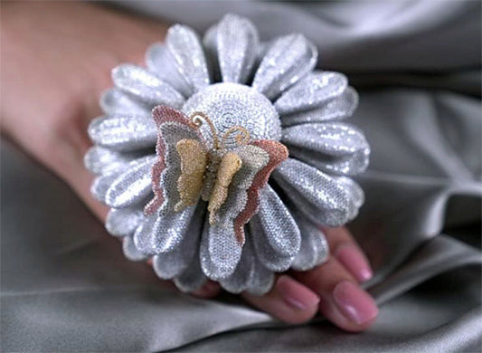 Close-up of a silver flower-shaped brooch with a butterfly design in the center, held in a hand.