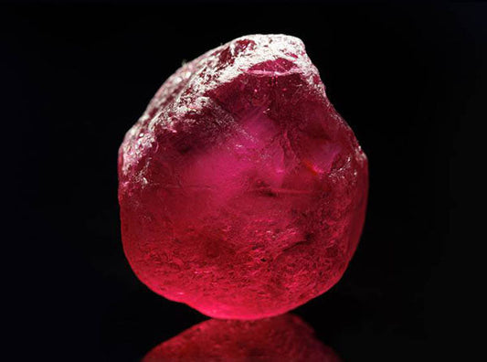 Raw uncut ruby gemstone with a rich red color, displayed against a dark background to highlight its natural texture and brilliance.