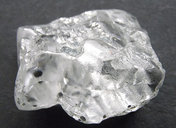 Rough, unpolished diamond crystal with clear and translucent facets, showing natural inclusions and a slightly opaque texture.