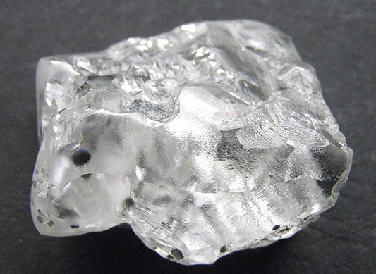 Rough, unpolished diamond crystal with clear and translucent facets, showing natural inclusions and a slightly opaque texture.