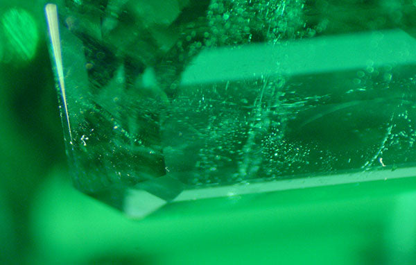 Close-up image of a green crystal with visible bubbles and internal reflections, showcasing its intricate texture and clarity.