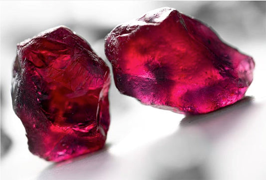 Close-up image of two raw ruby gemstones with deep red color, showing their natural crystal form and texture.