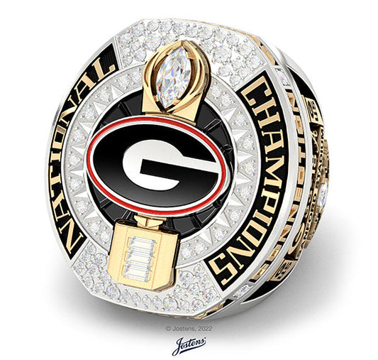 Close-up of a Georgia Bulldogs National Championship ring featuring a large diamond and the team's 'G' logo in the center. The ring is adorned with sparkling diamonds and the text 'NATIONAL CHAMPIONS' engraved on the band.