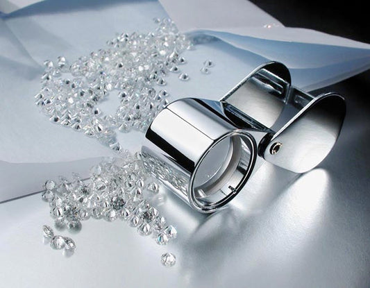 Silver jewelry ring magnifier with loose diamonds scattered on metallic surface.