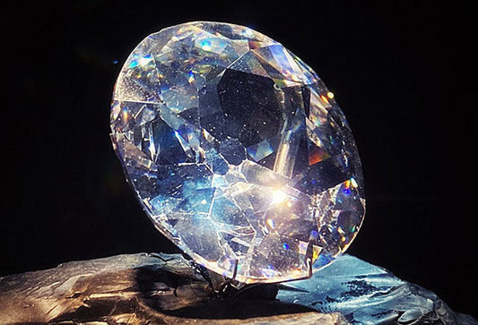 Close-up of a brilliant, faceted diamond resting on a stone, showcasing its sparkle and clarity under soft lighting.