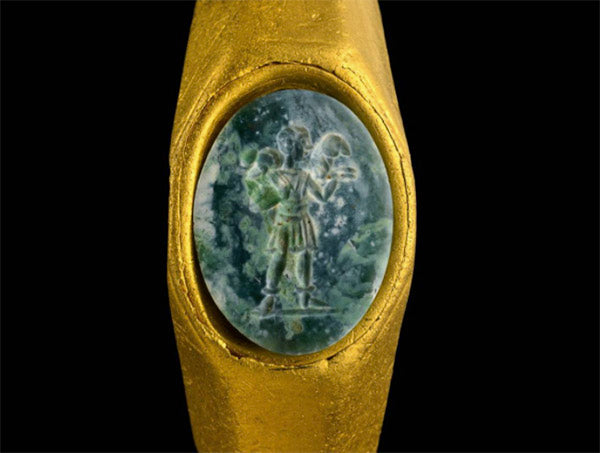 Close-up of an ancient gold ring featuring a carved green gemstone with a figure of a person holding items.