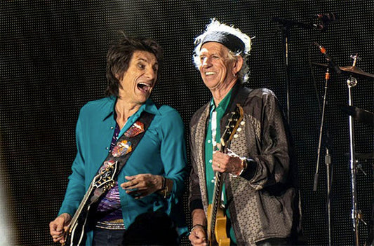 Ronnie Wood and Keith Richards of The Rolling Stones performing on stage, both smiling and playing electric guitars during a live concert.