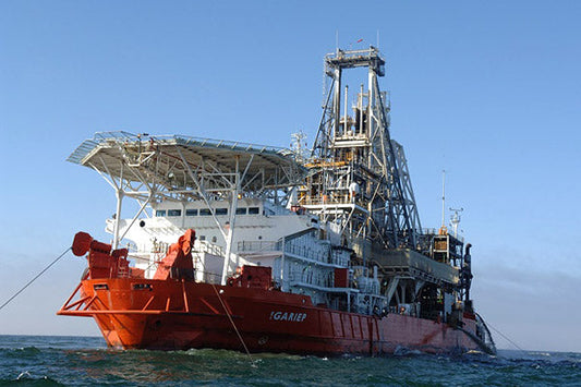 Oil drilling ship with towering rig structure on the ocean, used for offshore drilling and exploration, shown in clear daylight against a blue sky.