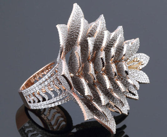 Close-up of an elegant silver and rose gold flower-shaped ring with intricate diamond-like detailing. The petals of the flower design are encrusted with sparkling stones, showcasing luxurious craftsmanship against a dark background.