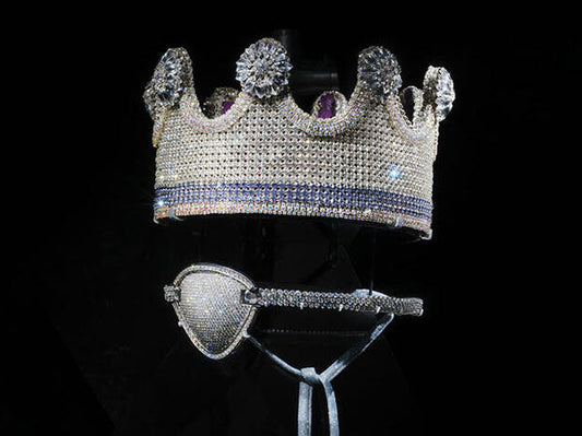 Diamond-studded crown and matching eye mask with purple and white gems, displayed against a dark background.
