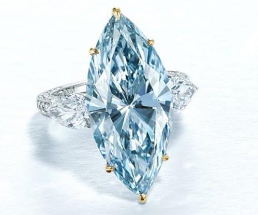 Marquise-shaped blue diamond engagement ring with side diamonds, set in white gold. The center diamond is large and sparkling, surrounded by smaller round diamonds on either side.