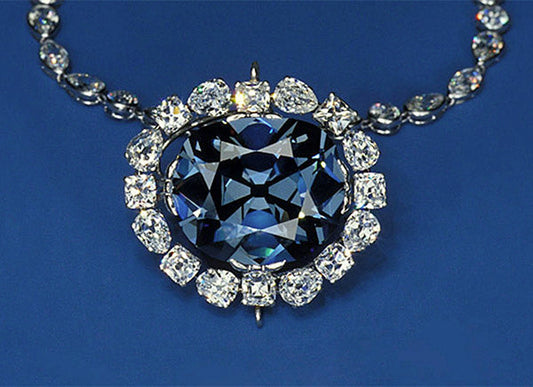 Close-up of the Hope Diamond, a large blue diamond surrounded by smaller white diamonds, set in a necklace against a blue background.