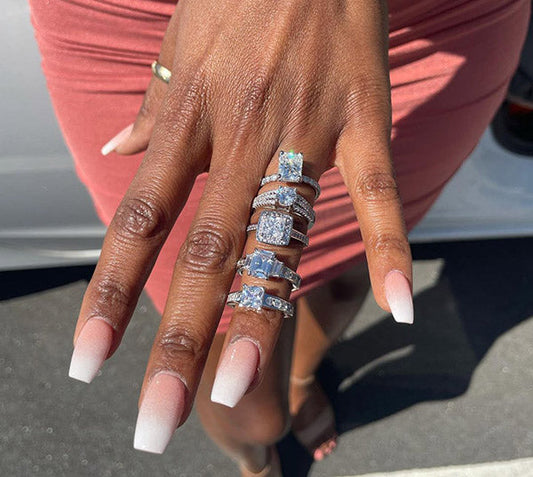 Close-up of a hand wearing multiple sparkling diamond rings stacked on each finger, with a stylish French manicure.